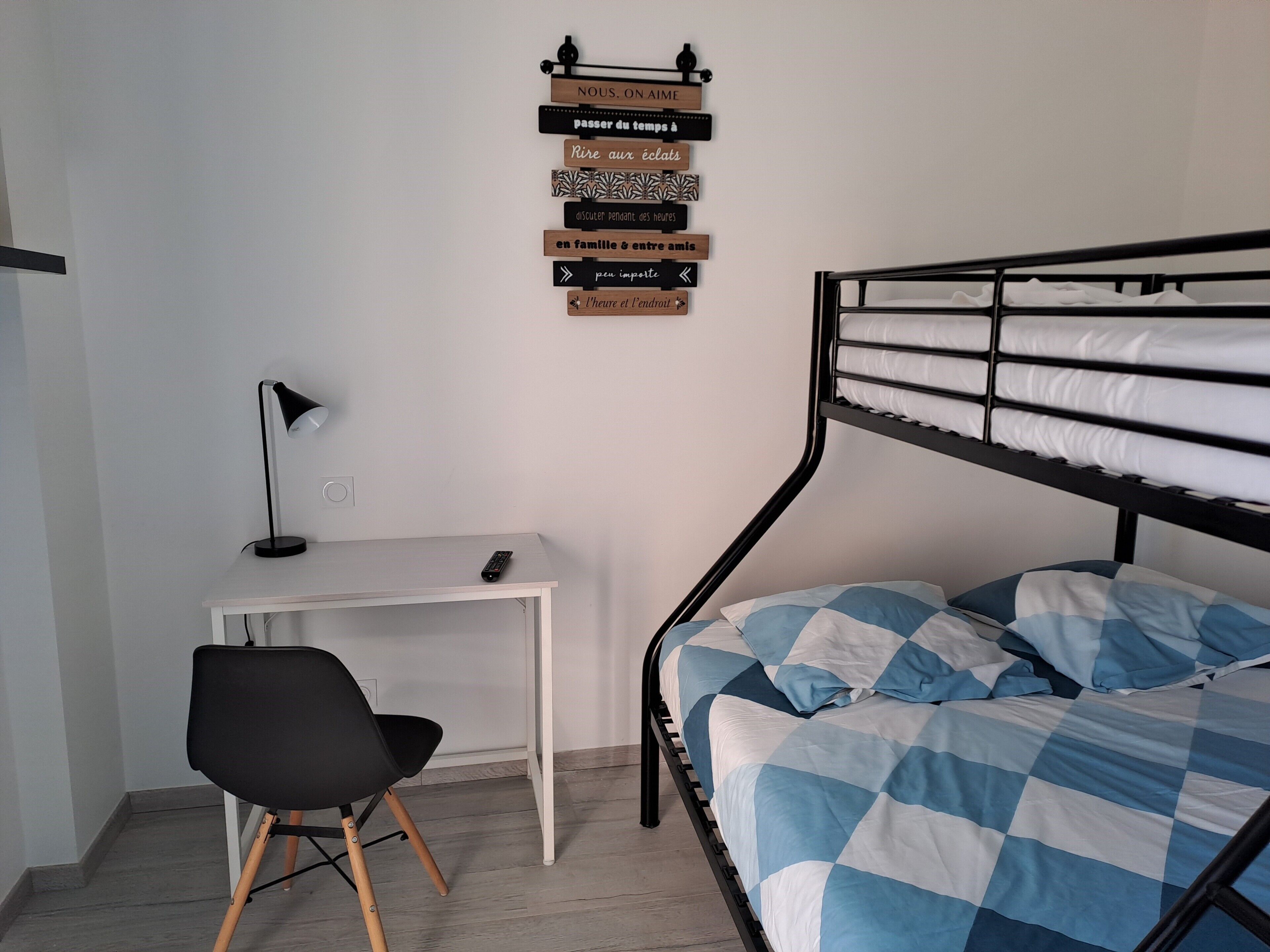 A dormitory room with a bunk bed, a desk with a chair, a lamp, and a wall with motivational signs.