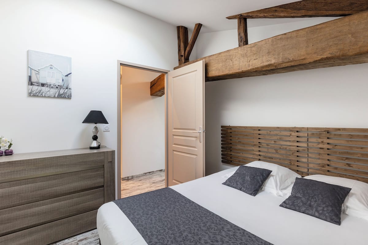 Un dormitorio con cama, mesita de noche, lámpara y una puerta que da a otra habitación.