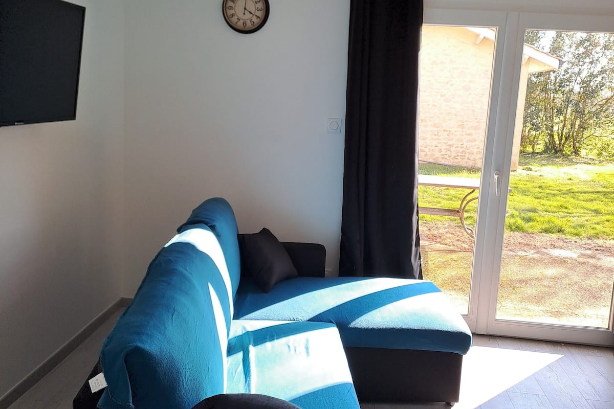 Una habitación con un sofá azul, un reloj de pared y un ventanal corredera que da a un jardín.