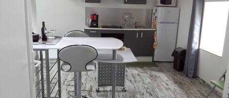 A compact kitchen with a white countertop, two bar stools, a microwave, and a refrigerator.