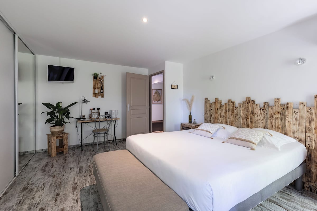 Un dormitorio con cama, escritorio, silla, televisión y planta.