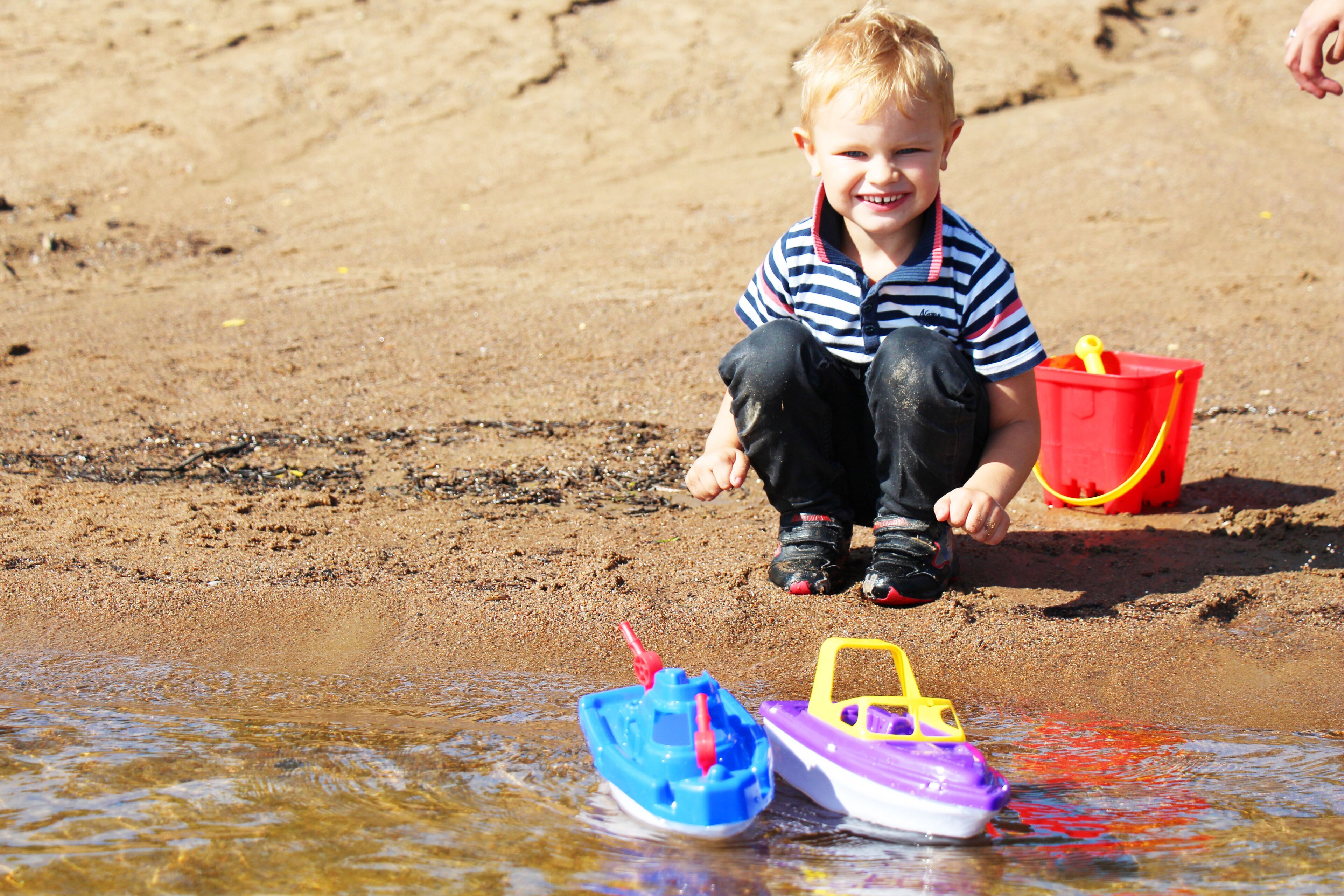 A child playing with toy boats on a sandy beach.