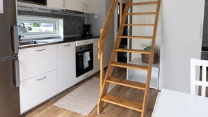 A modern kitchen with white cabinets, stainless steel appliances, a wooden ladder, and a view of the outside. - Evedals Camping (Växjö)