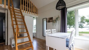 A modern interior with a wooden ladder, white furniture, and a view of a lake through large windows. - Evedals Camping (Växjö)