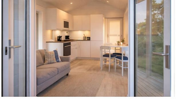 A modern interior with a sofa, dining table, chairs, and a kitchen area. - Evedals Camping (Växjö)