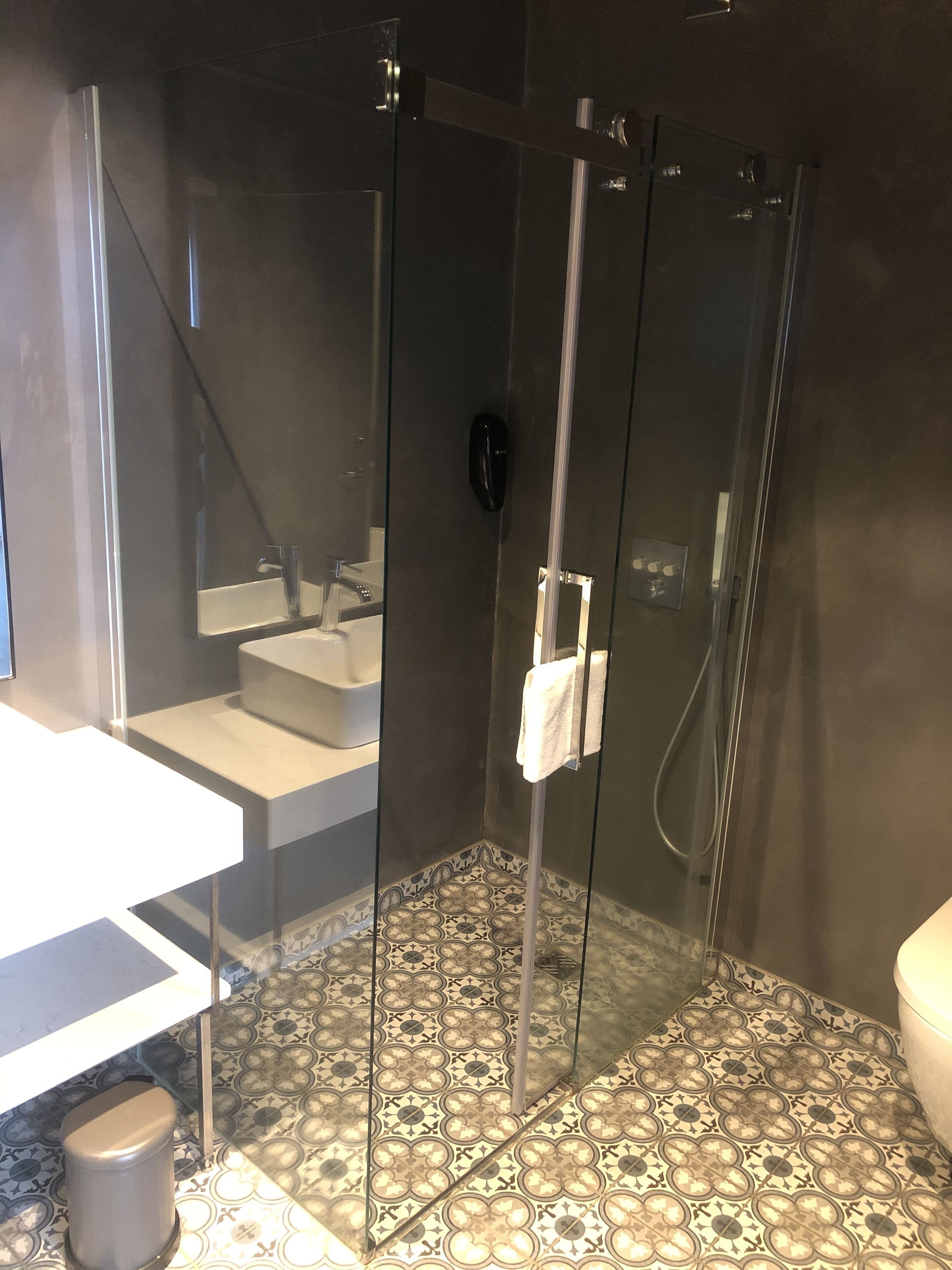 A modern bathroom with a glass-enclosed shower, a white sink, and patterned floor tiles.