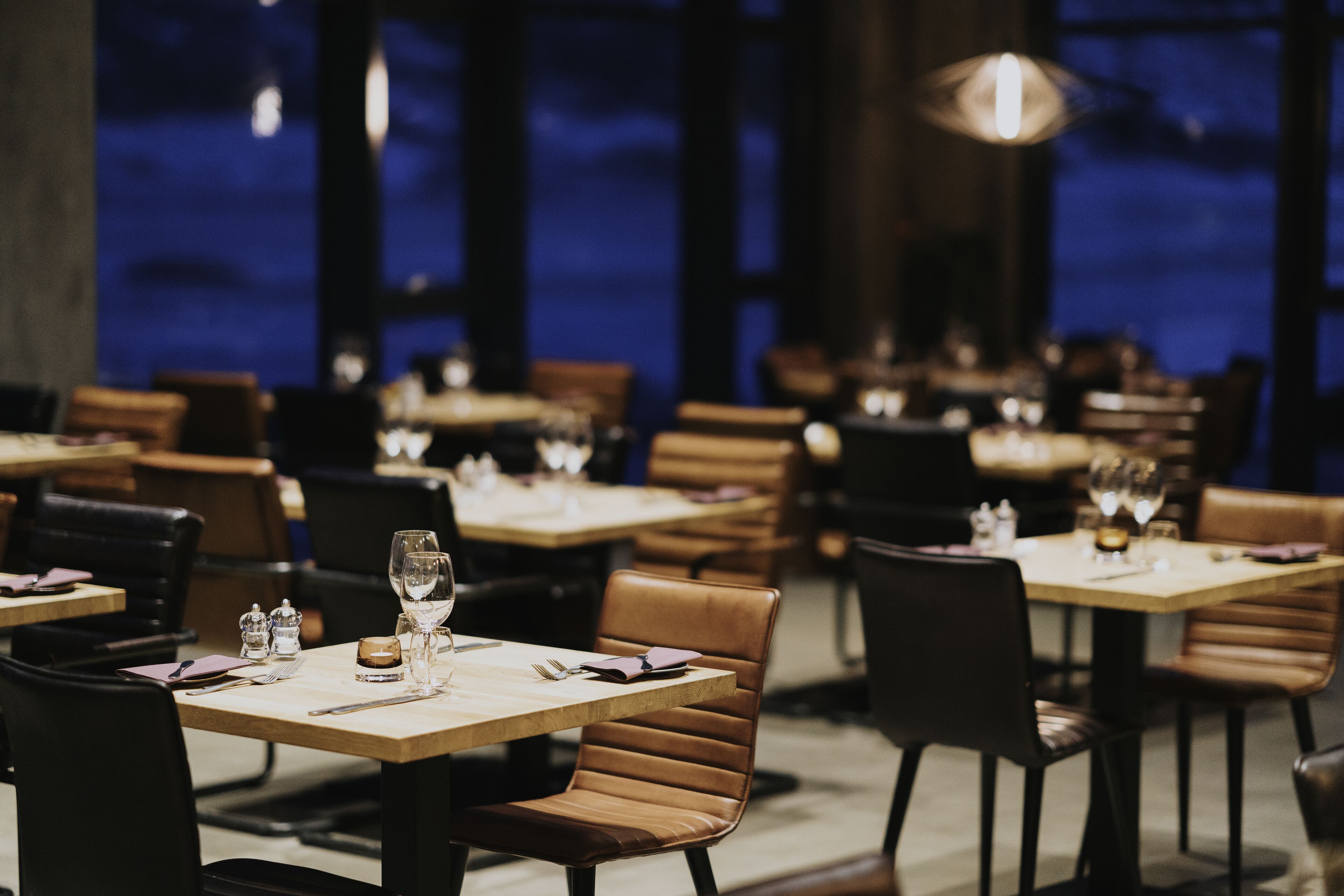 Ein Restaurantinneres mit gedeckten Tischen, das durch ein modernes Design mit Holztischen und Ledersesseln besticht.