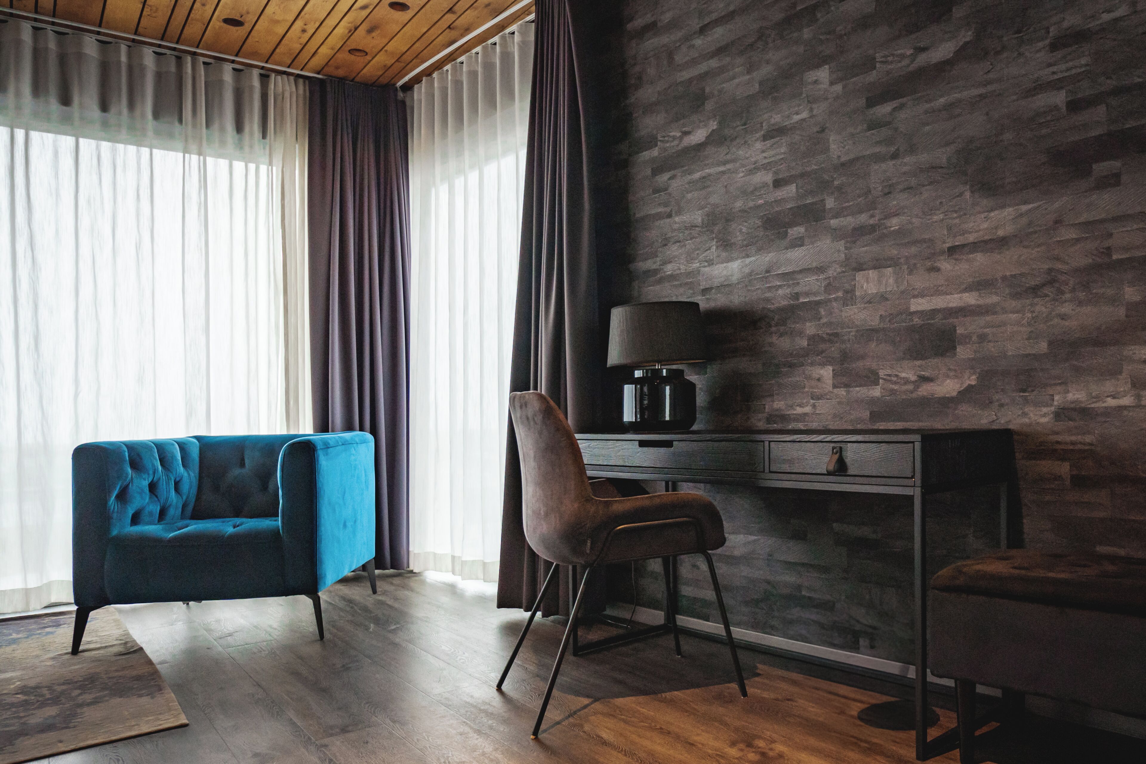 Une pièce avec un canapé bleu, un fauteuil, un bureau avec une lampe et un mur à la texture de pierre.