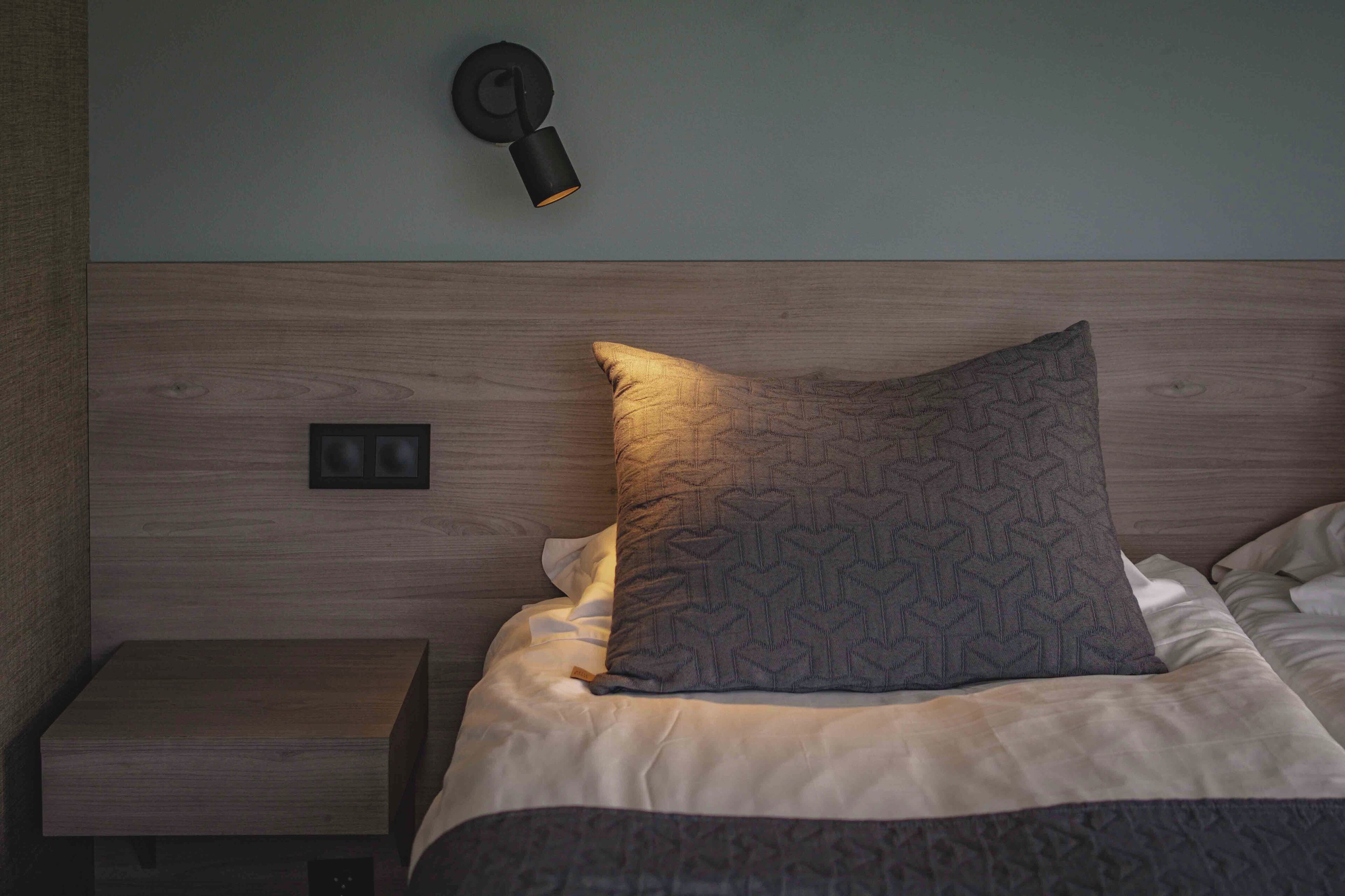 A neatly made bed with a patterned pillow and a wall-mounted light fixture.