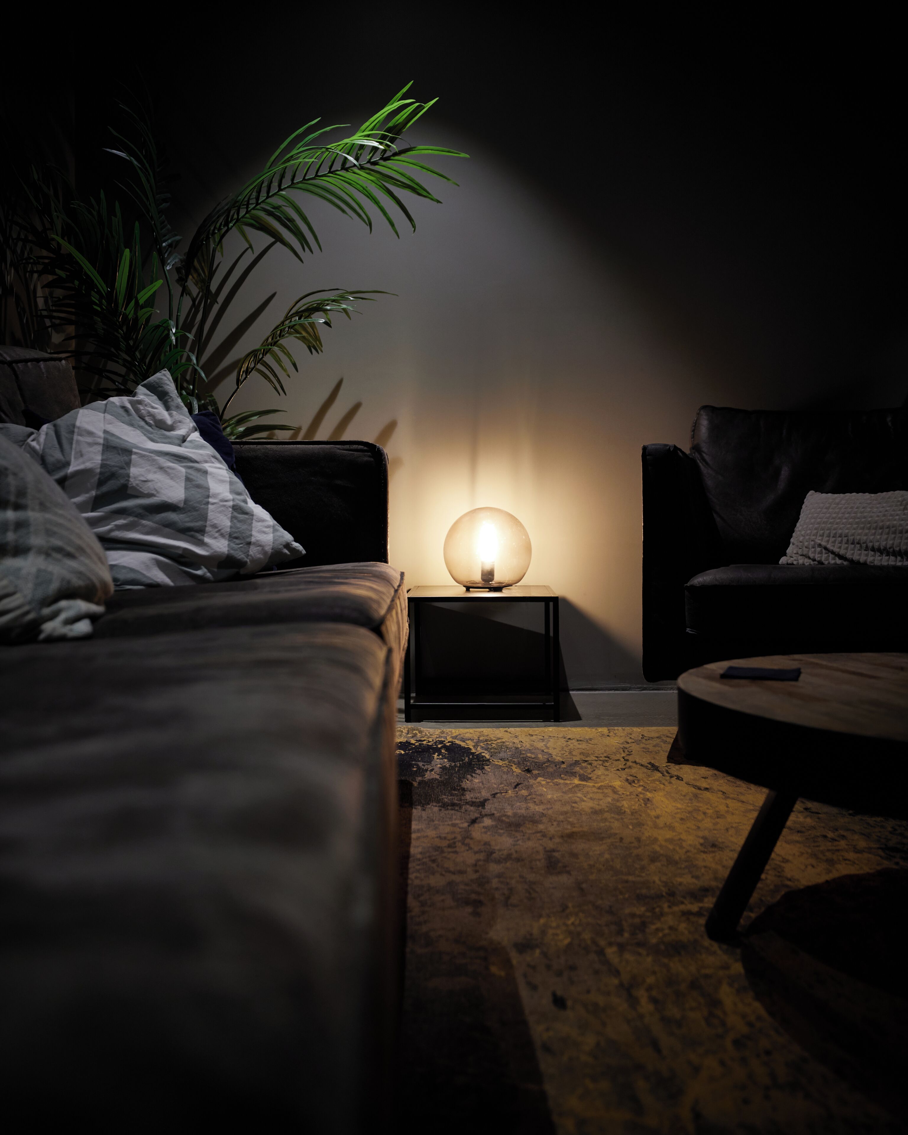 A dimly lit room with a sofa, a small table, and a lamp on a side table.