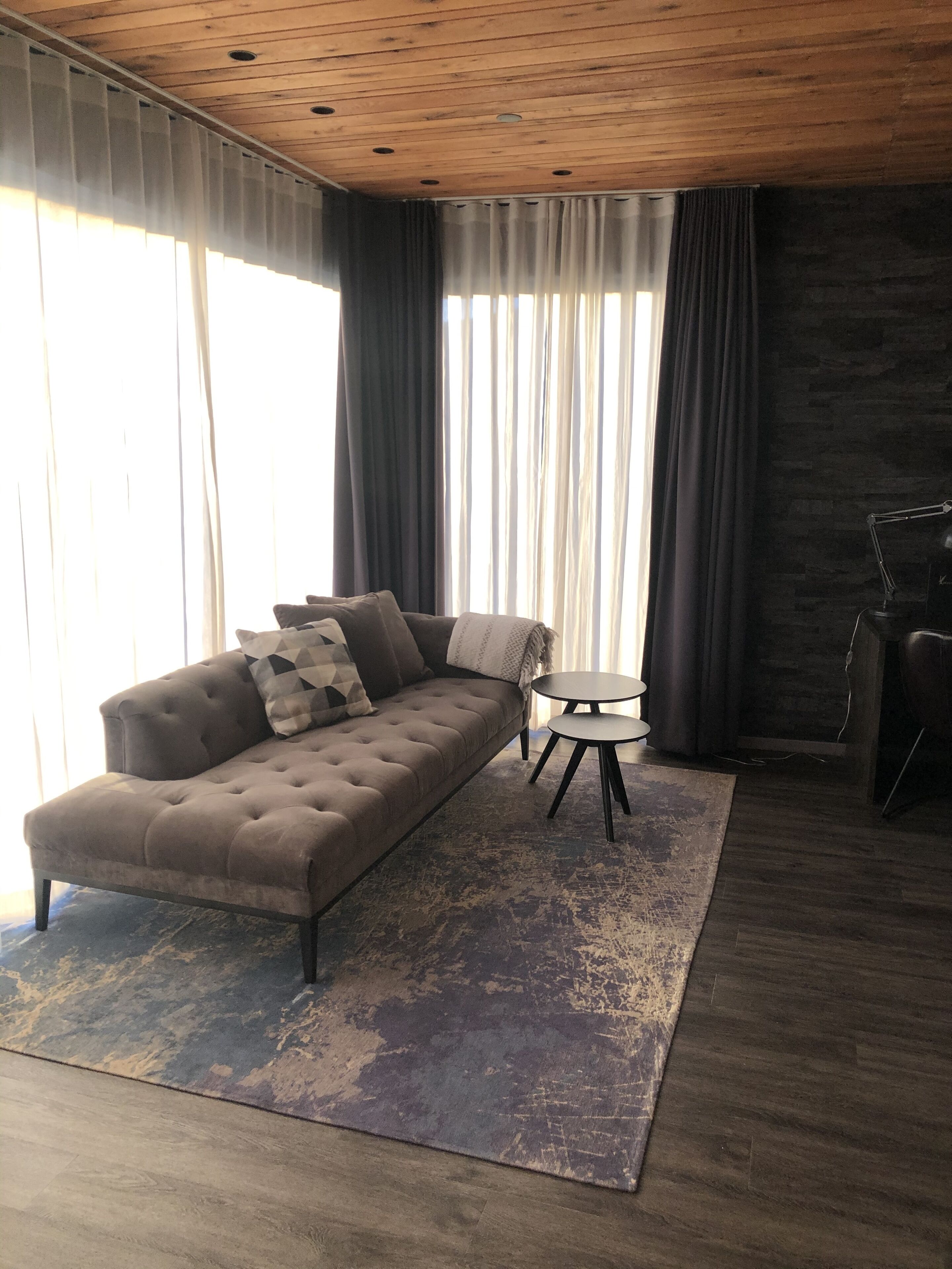 A modern living room with a tufted sofa, a small round table, and a large window with curtains.