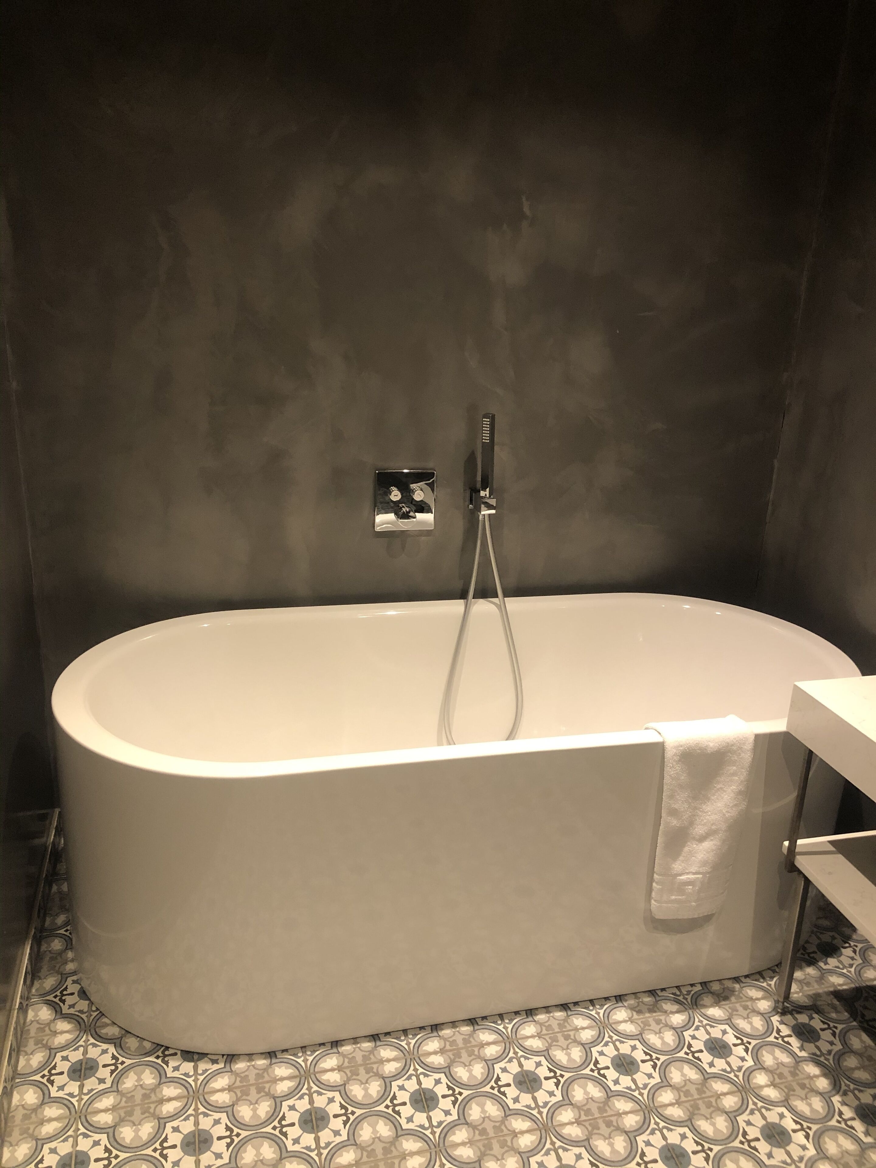 Un baño moderno con una bañera independiente, un cabezal de ducha en la pared y un suelo de baldosas con diseño.