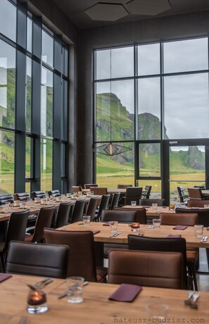 Un restaurante con amplios ventanales que ofrece vistas a colinas verdes. Las mesas están dispuestas con copas y cubiertos.