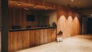 A reception area with wooden paneling, a reception desk, a flat-screen TV, and a floor lamp. - Hótel Kría (Vik I Myrdal)