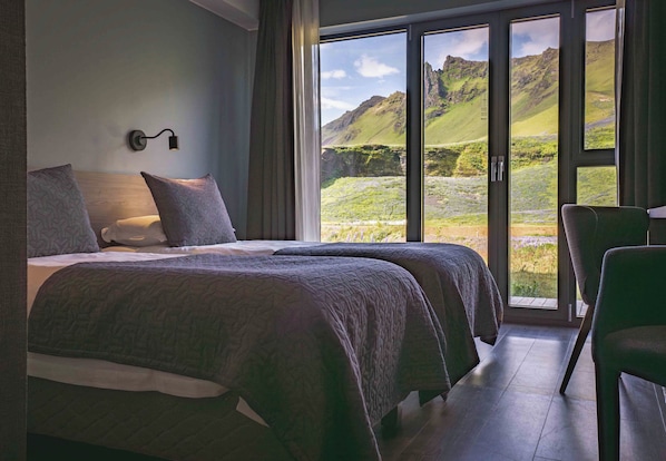 A bedroom with two beds, a large window with a mountain view, and a chair.