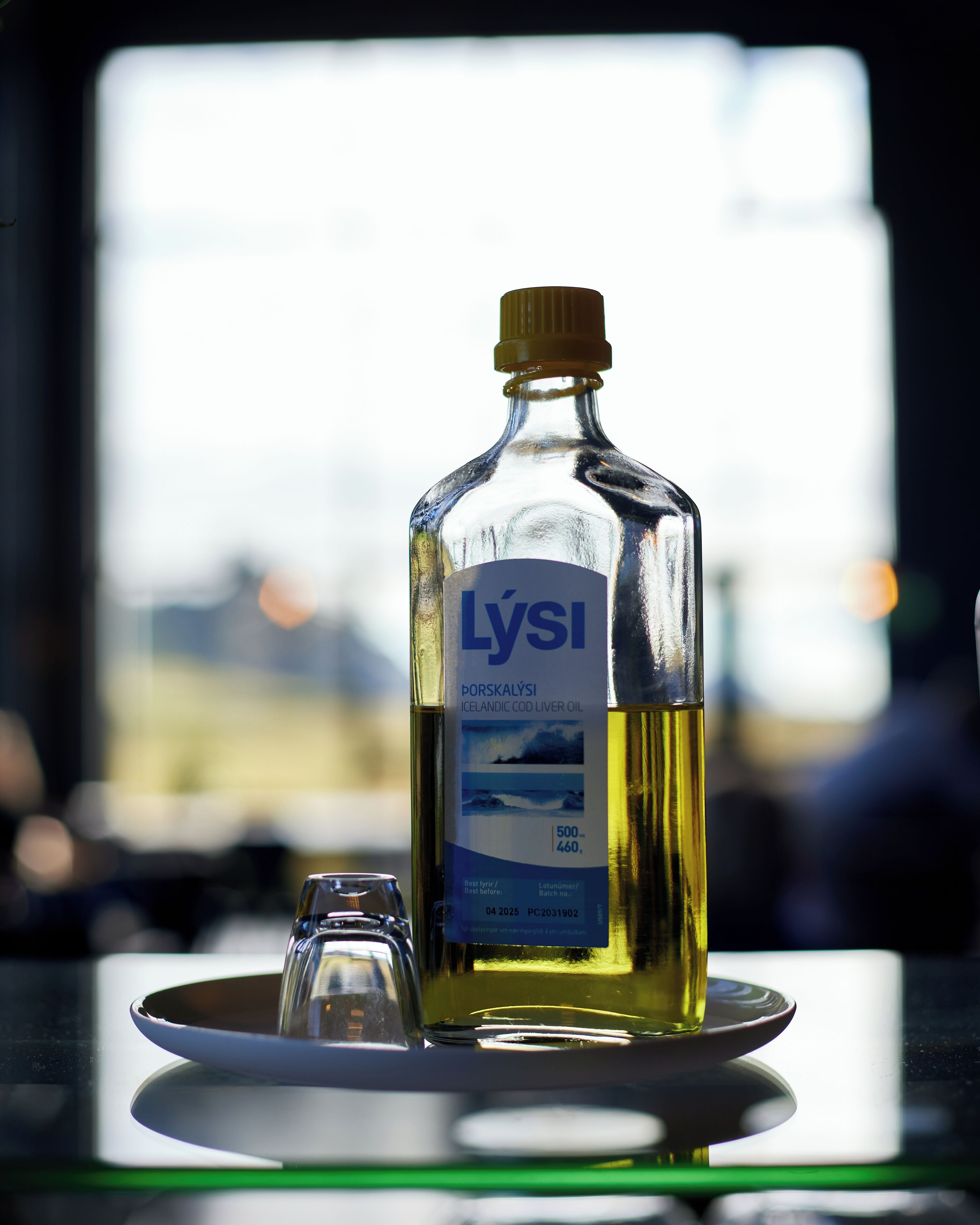 A bottle of Lýsi Icelandic cod liver oil on a plate with a glass beside it.