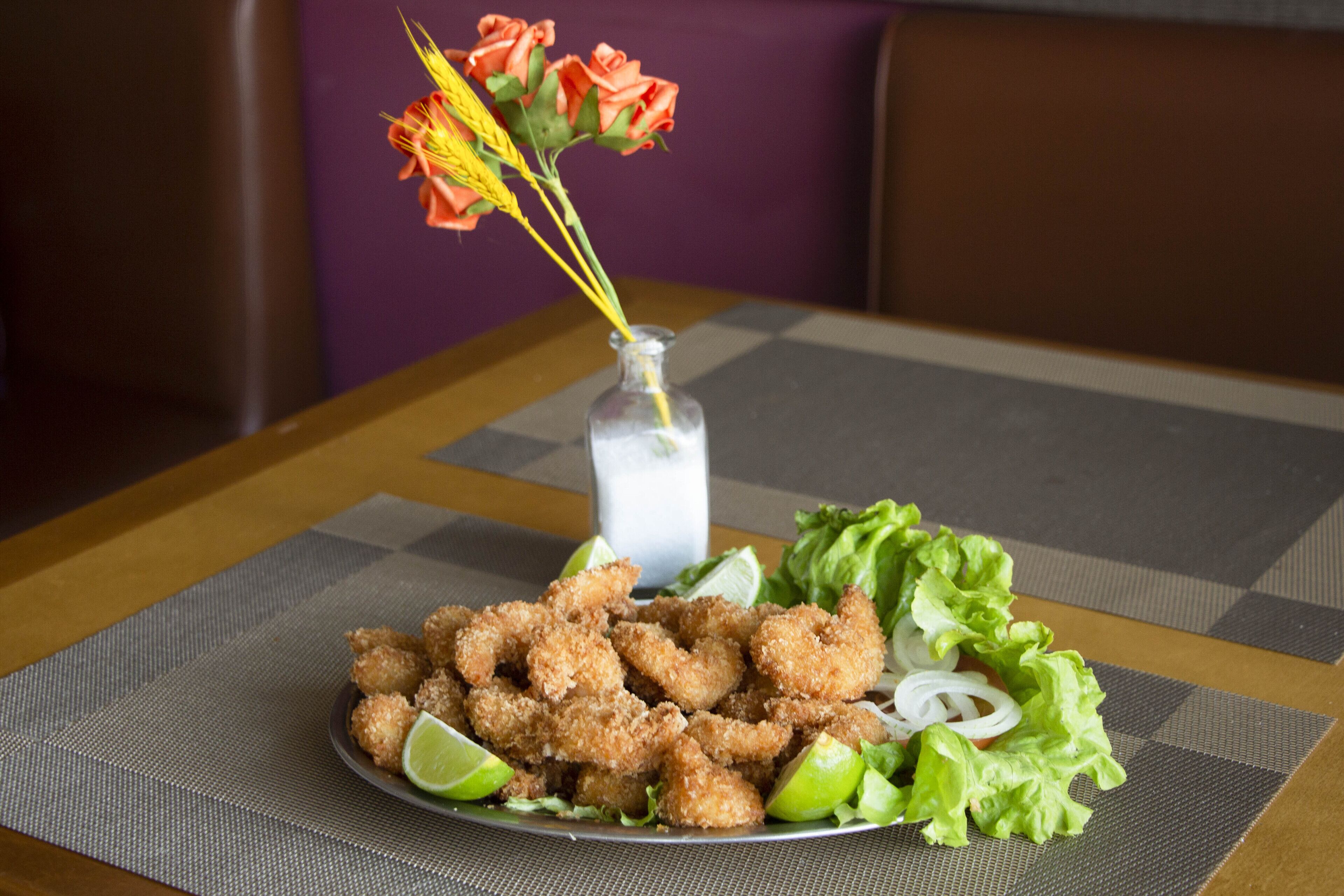 Un plato de camarones fritos con cuñas de limón y lechuga sobre un mantel a cuadros.
