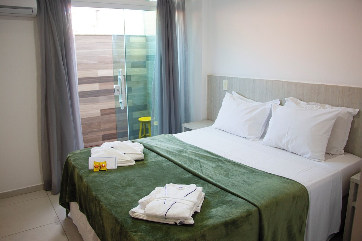 A hotel room with a bed, green bedspread, white pillows, and a glass door leading to a balcony.