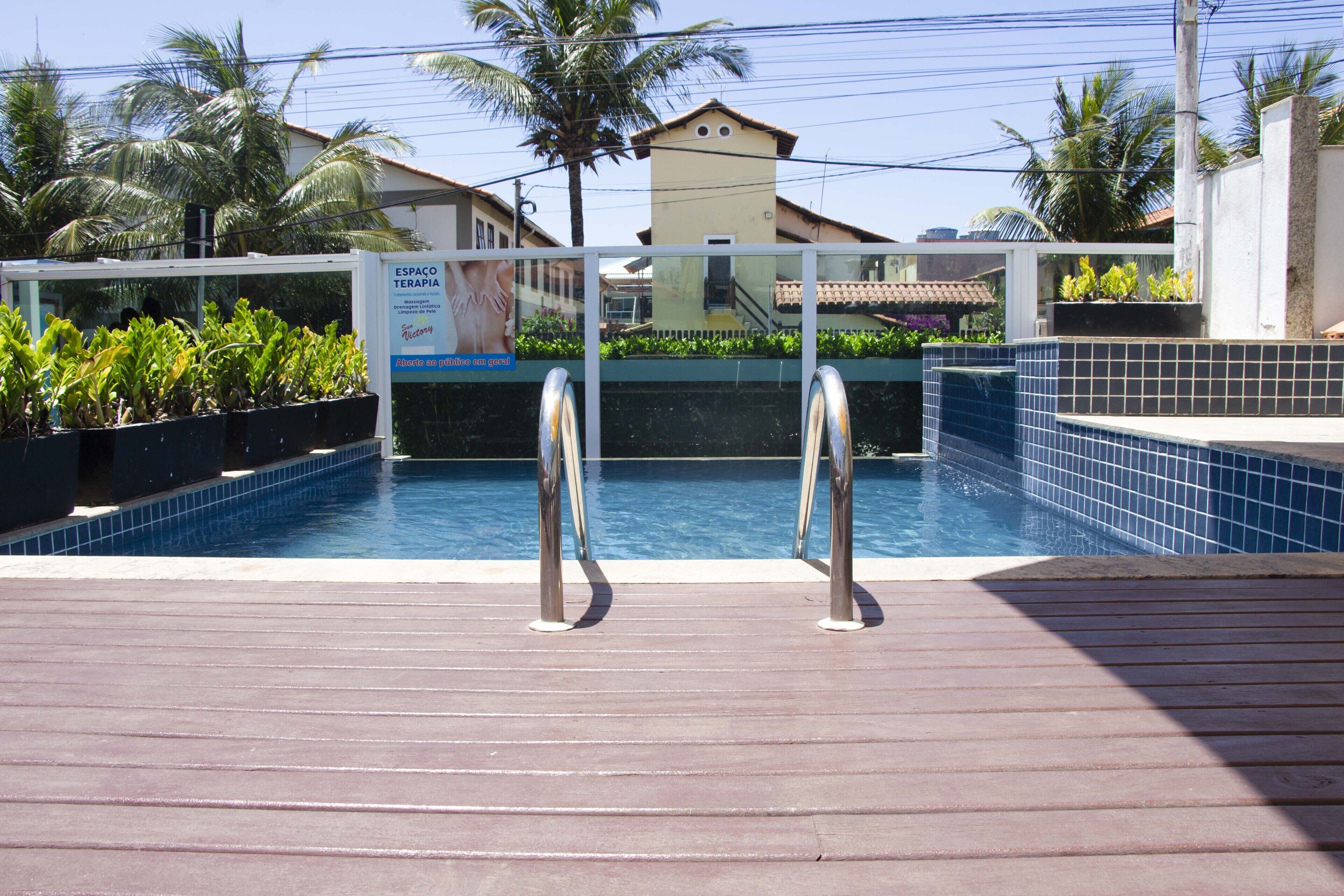 A swimming pool with metal railings, surrounded by potted plants and a tiled deck.