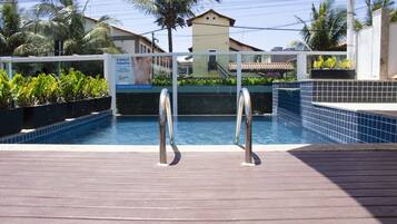 A swimming pool with metal railings, surrounded by potted plants and a tiled deck.