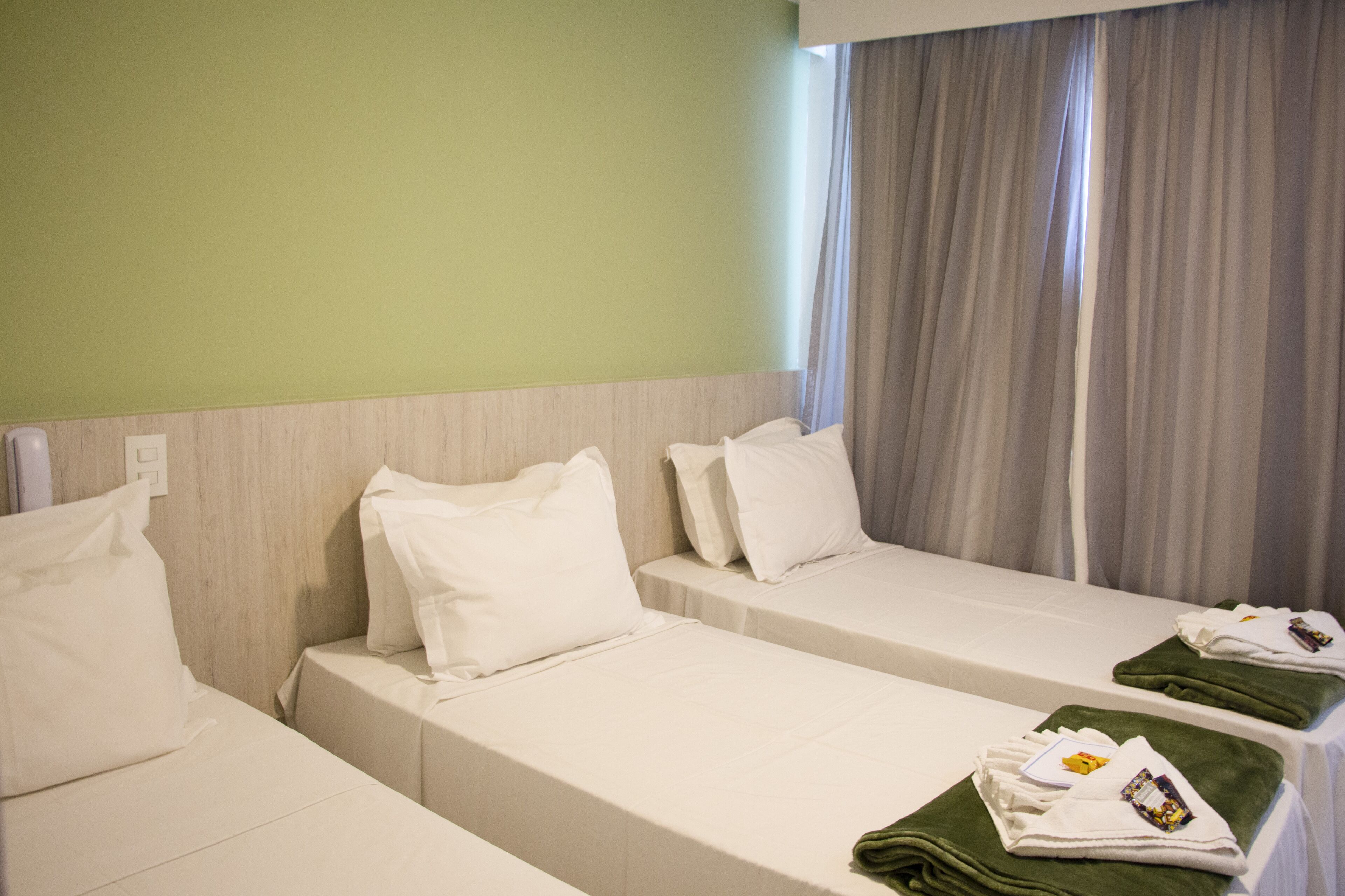 A hotel room with two single beds, a wooden headboard, a green towel, and a window with curtains.