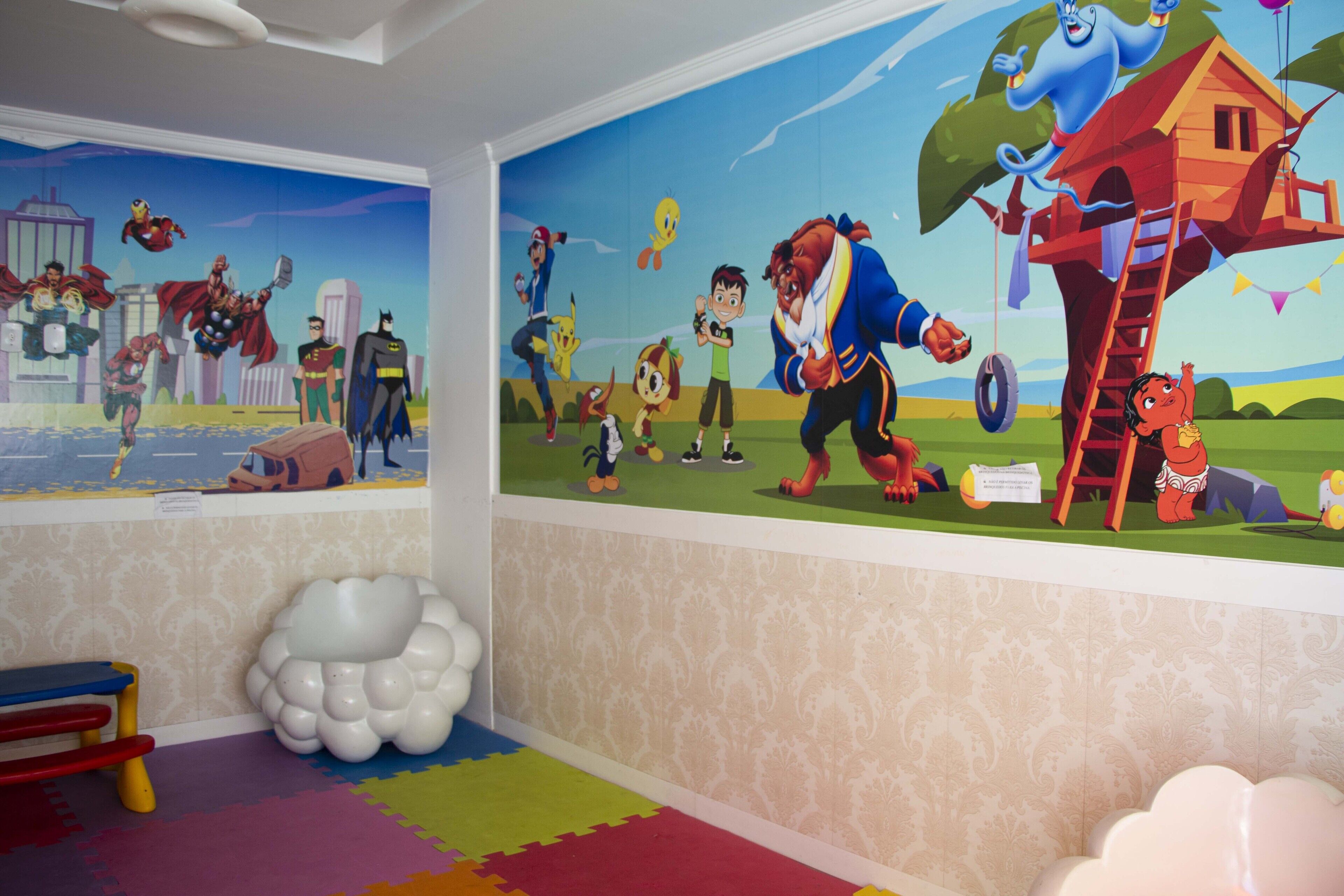 A children's room with a mural of superheroes and animated characters, a colorful play mat, and a cloud-shaped decoration.
