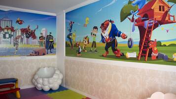 A children's room with a mural of superheroes and animated characters, a colorful play mat, and a cloud-shaped decoration.