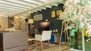Una sala de estar moderna con un sofá, una butaca, un televisor, plantas decorativas y obras de arte en las paredes.