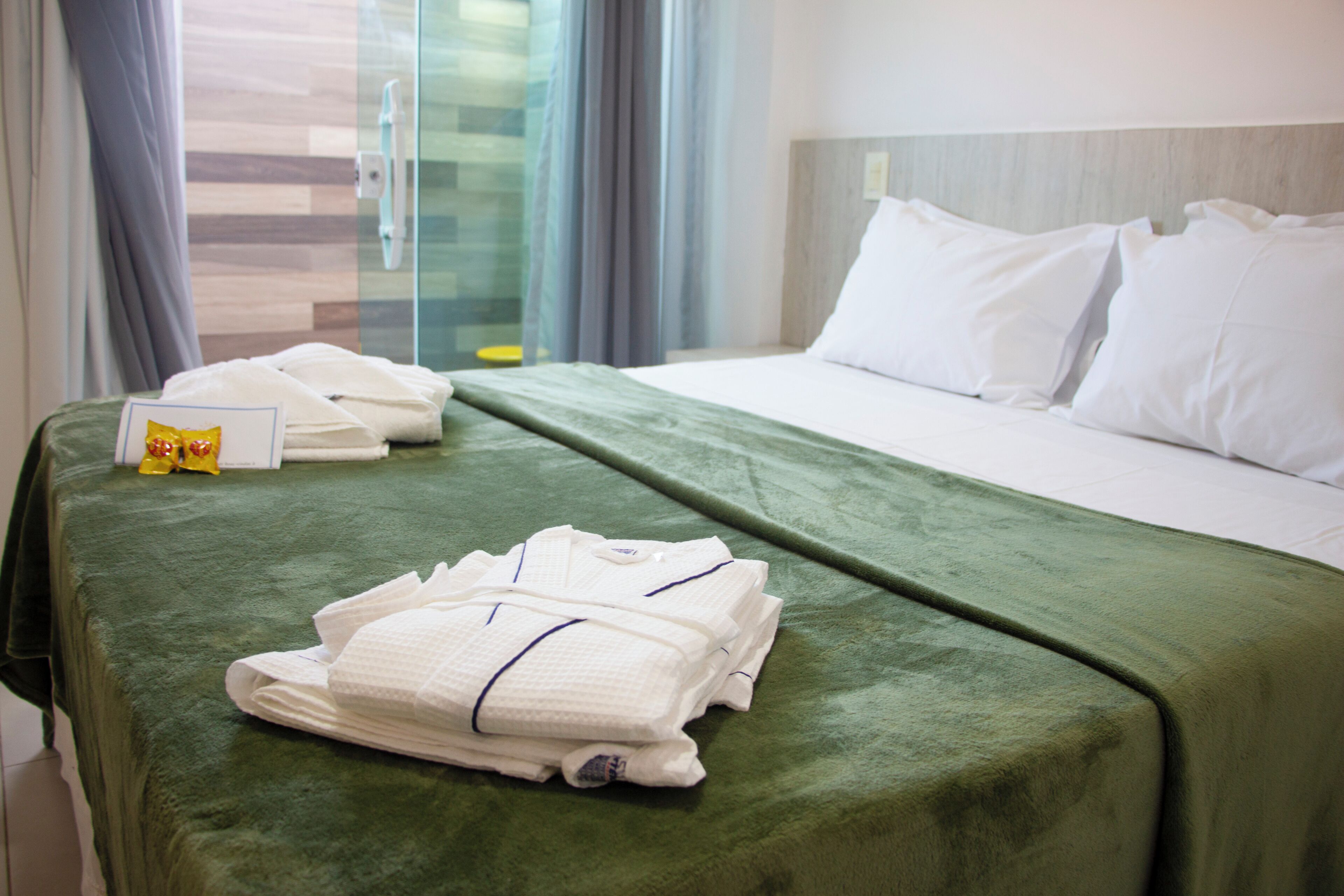 A hotel room with a neatly made bed, a green bedspread, and a set of folded towels on the bed.