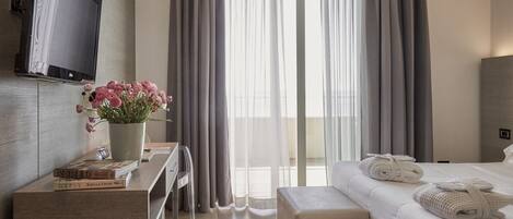 Habitación de hotel con cama, escritorio con un jarrón de flores, televisor de pantalla plana y ventana con cortinas.