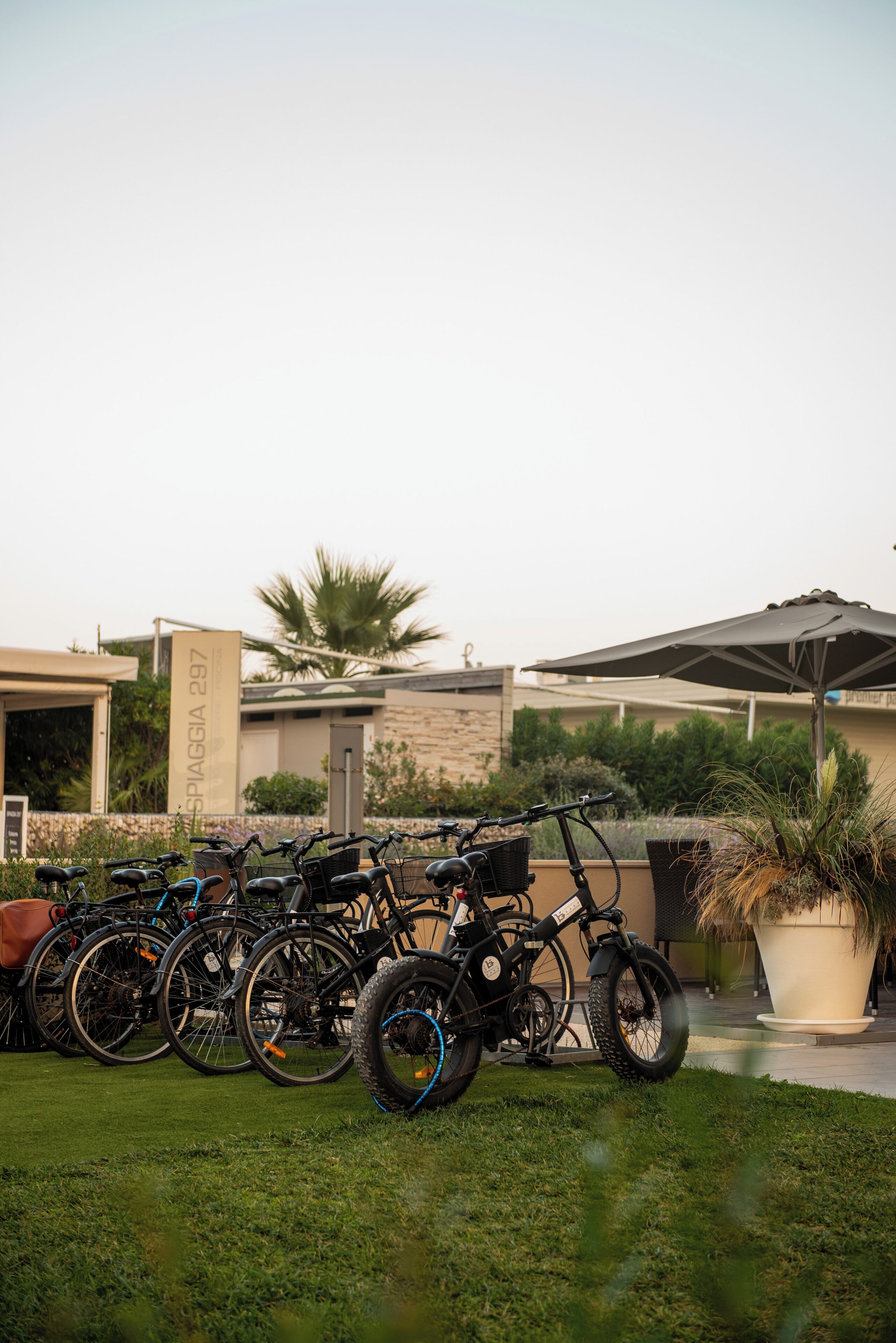 A row of bicycles parked in a grassy area with a building in the background.