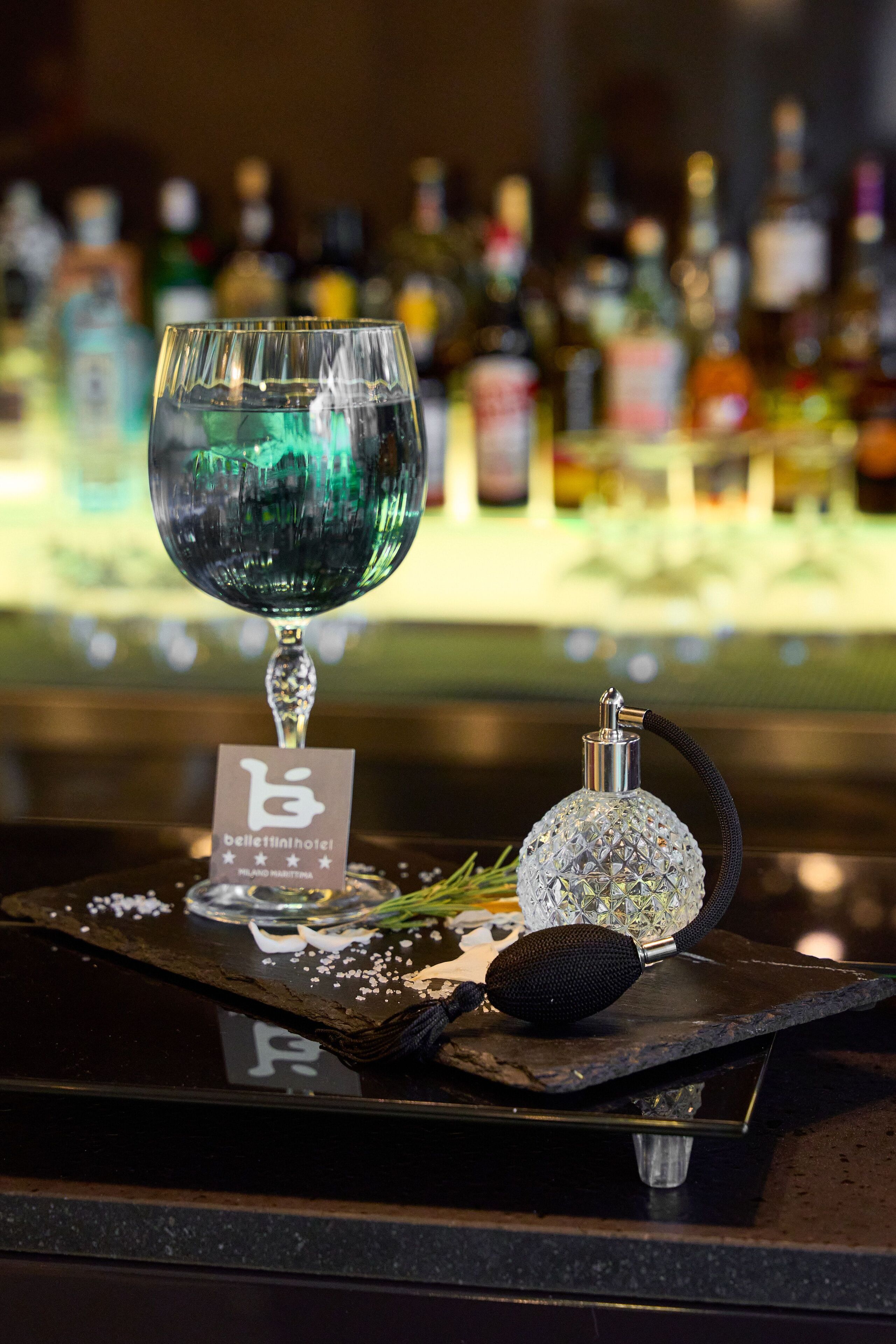 Un bar con una copa de líquido verde, un decantador de cristal y una botella de licor sobre una bandeja con un cartel de hotel.