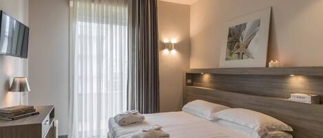 Una habitación de hotel con una cama, una mesita de noche, una lámpara y un cuadro en la pared.