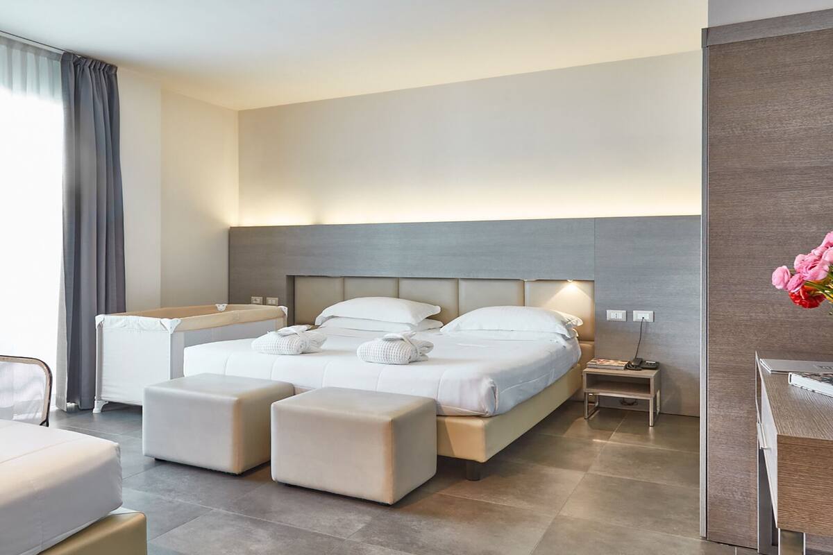 Ein modernes Hotelzimmer mit einem großen Bett, zwei Nachttischen, einem kleinen Schreibtisch und einem Sessel.