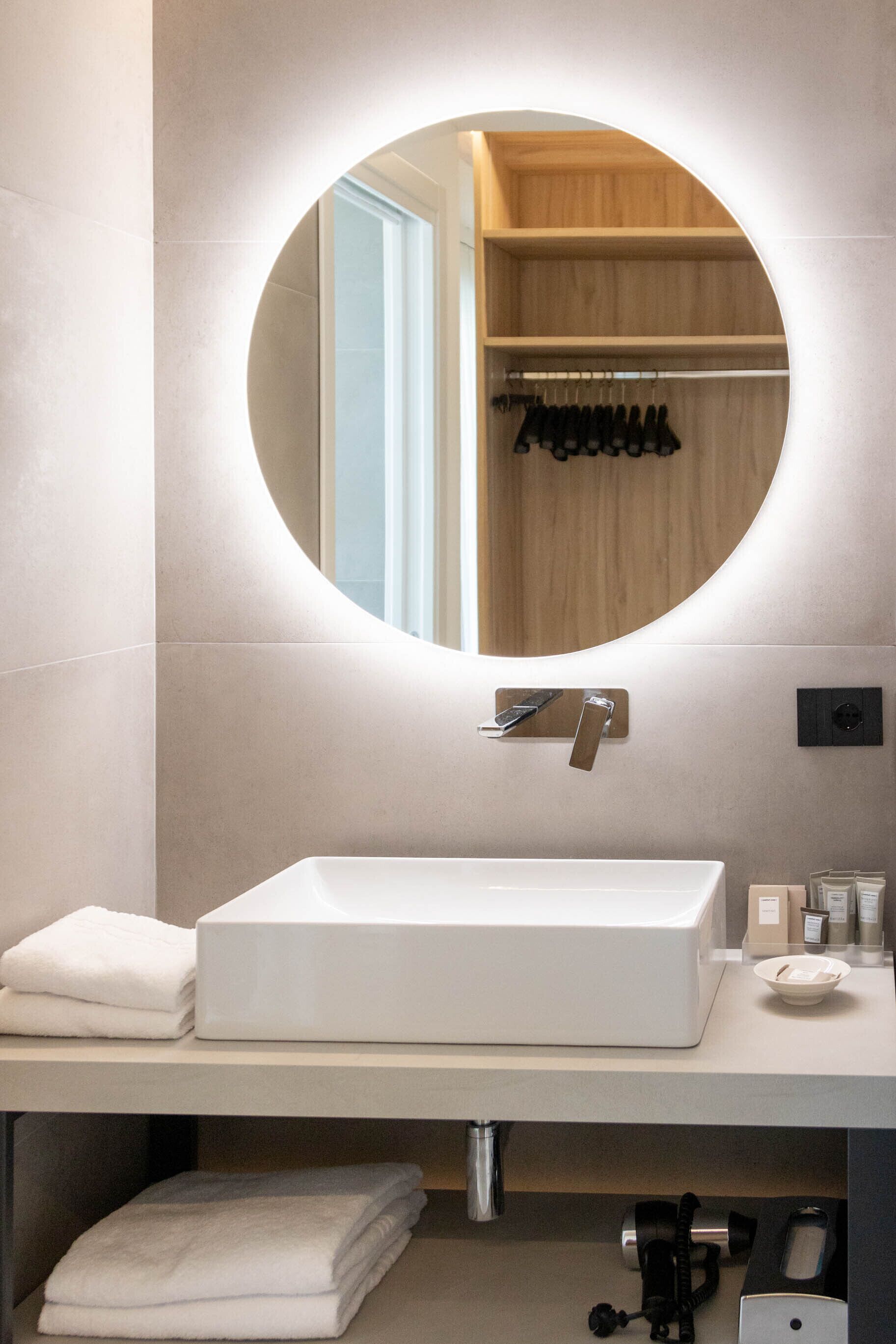 A modern bathroom with a round mirror, a white sink, and neatly folded towels on the counter.