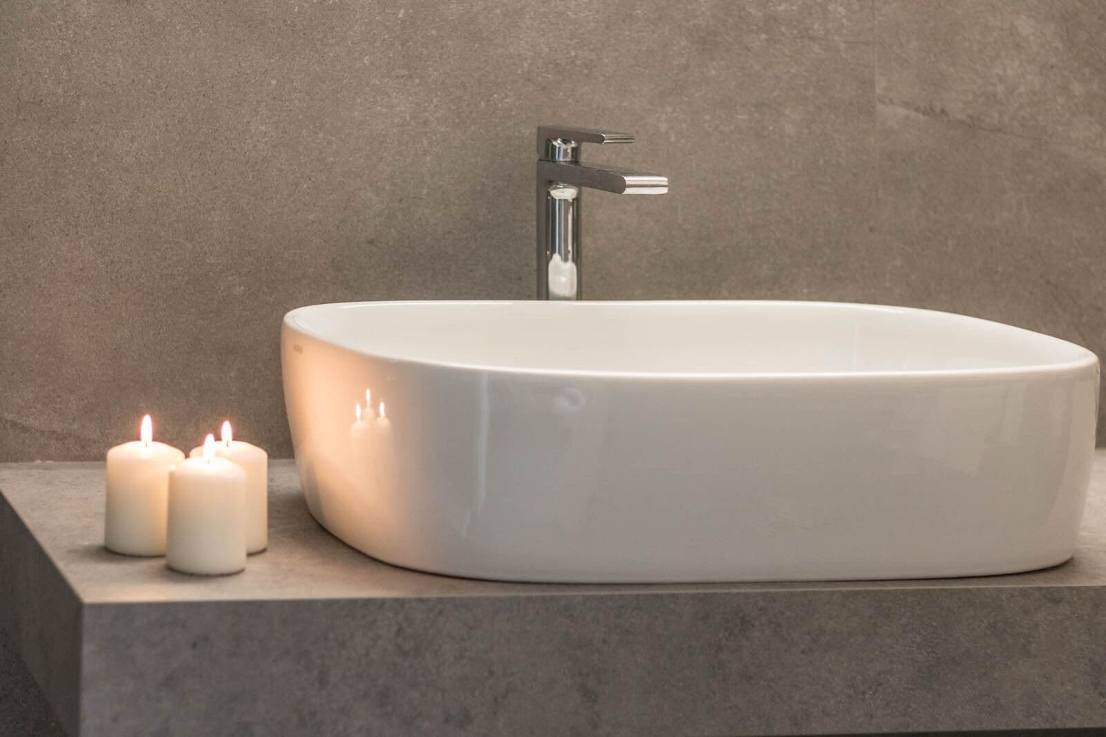 A modern bathroom with a white oval sink, a faucet, and two lit candles on a countertop.