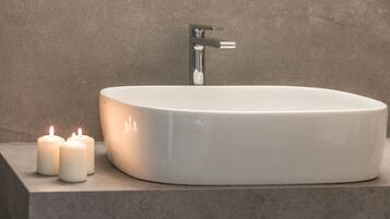 A modern bathroom with a white oval sink, a faucet, and two lit candles on a countertop.