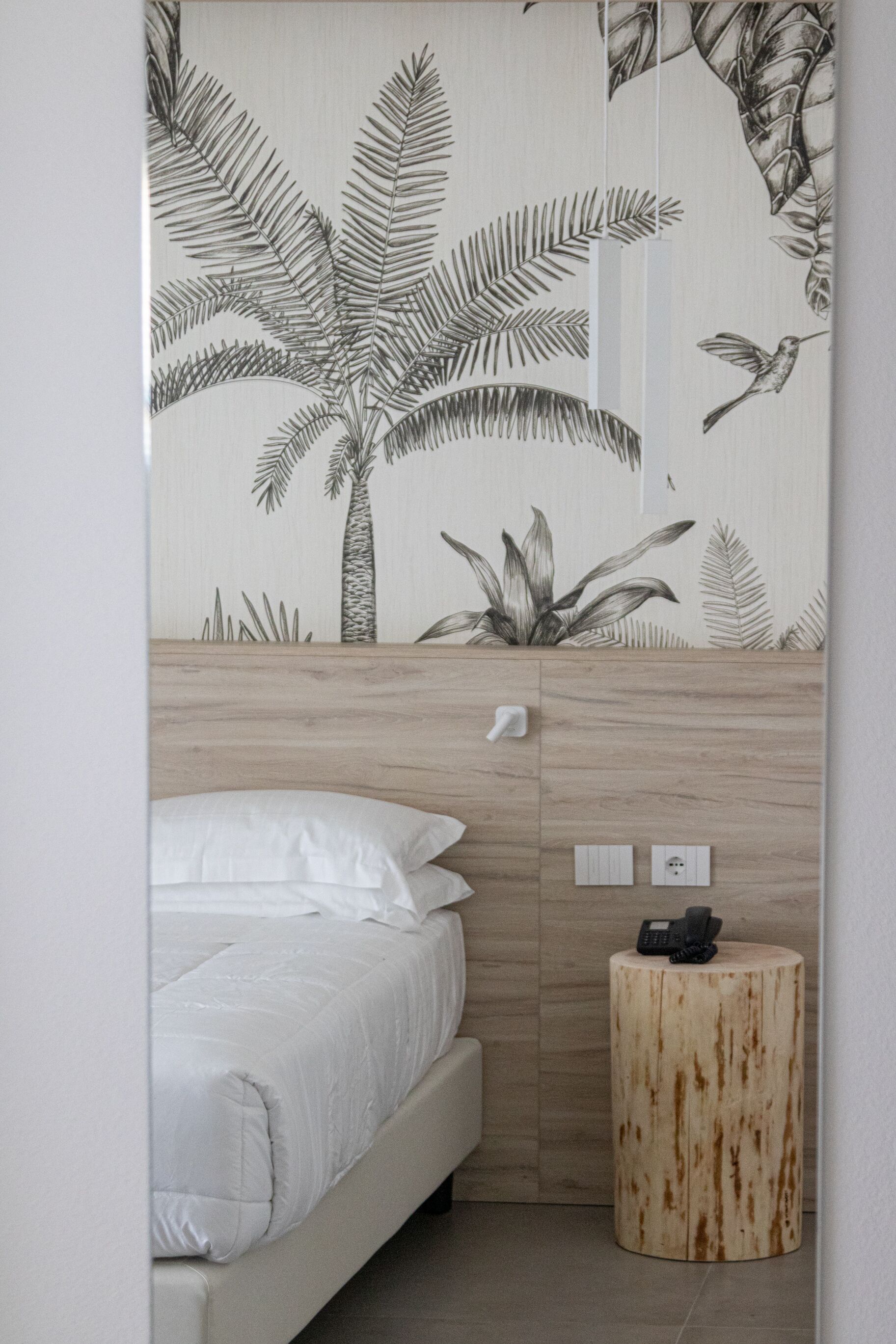 A bedroom with a bed, a bedside table, and a wall with a tropical leaf pattern.