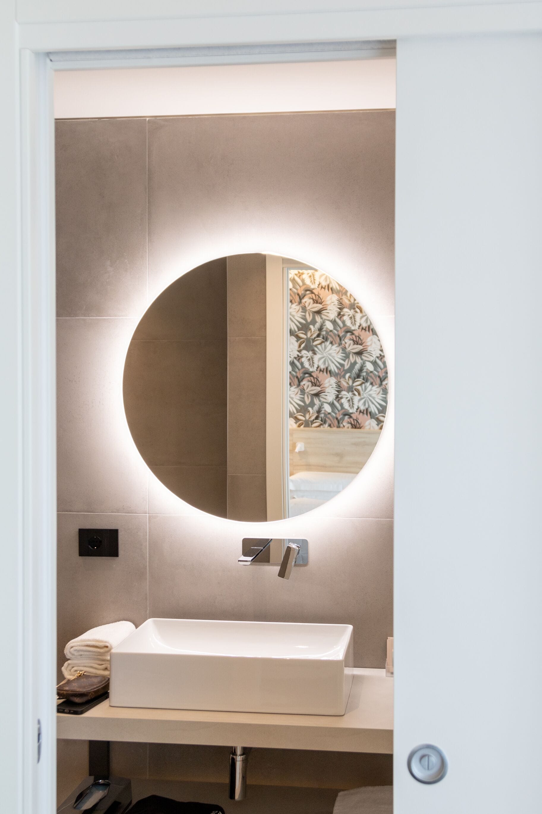 Une salle de bain avec un miroir rond, un lavabo blanc et un porte-serviettes.