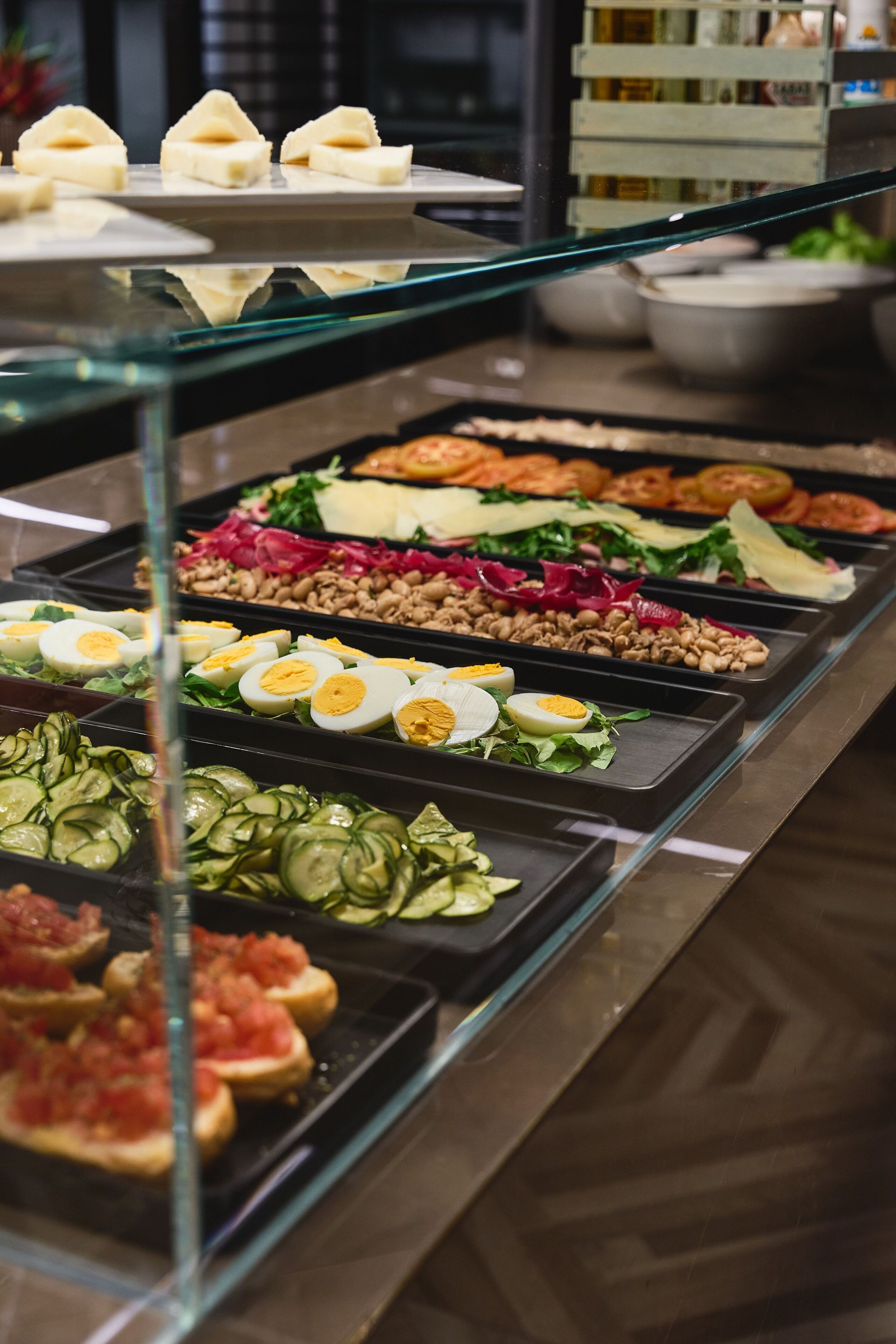 A buffet with various food items including sliced cucumbers, tomatoes, eggs, and leafy greens.