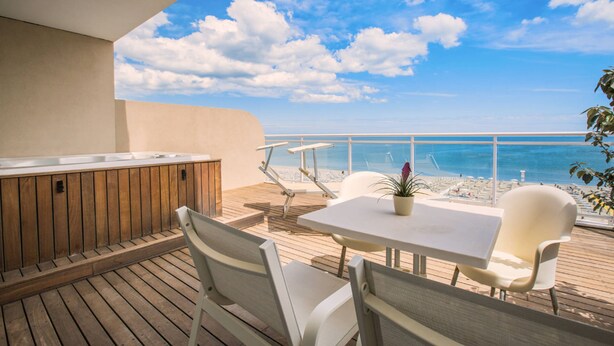 Una terraza de madera con mesa y sillas, un jacuzzi y vistas a la playa y el océano.