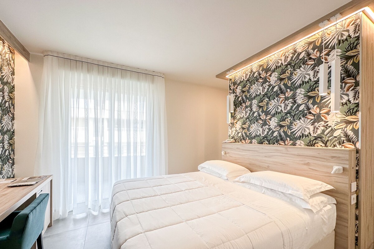 Un dormitorio moderno con una cama grande, un escritorio y una ventana con cortinas traslúcidas.