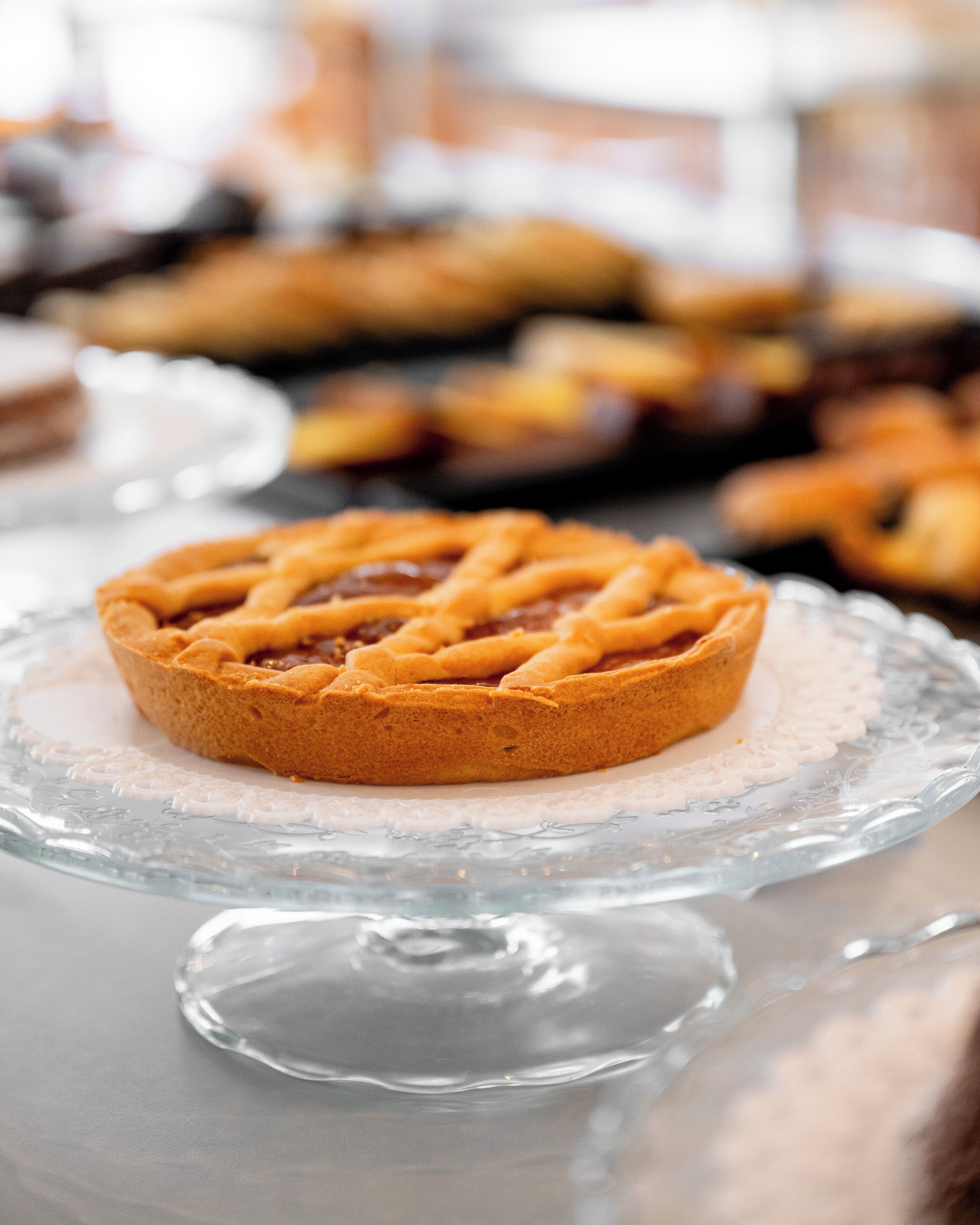 A glass pie dish with a lattice-topped pie on a reflective surface.