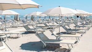 Una playa con filas de tumbonas blancas y sombrillas grandes.