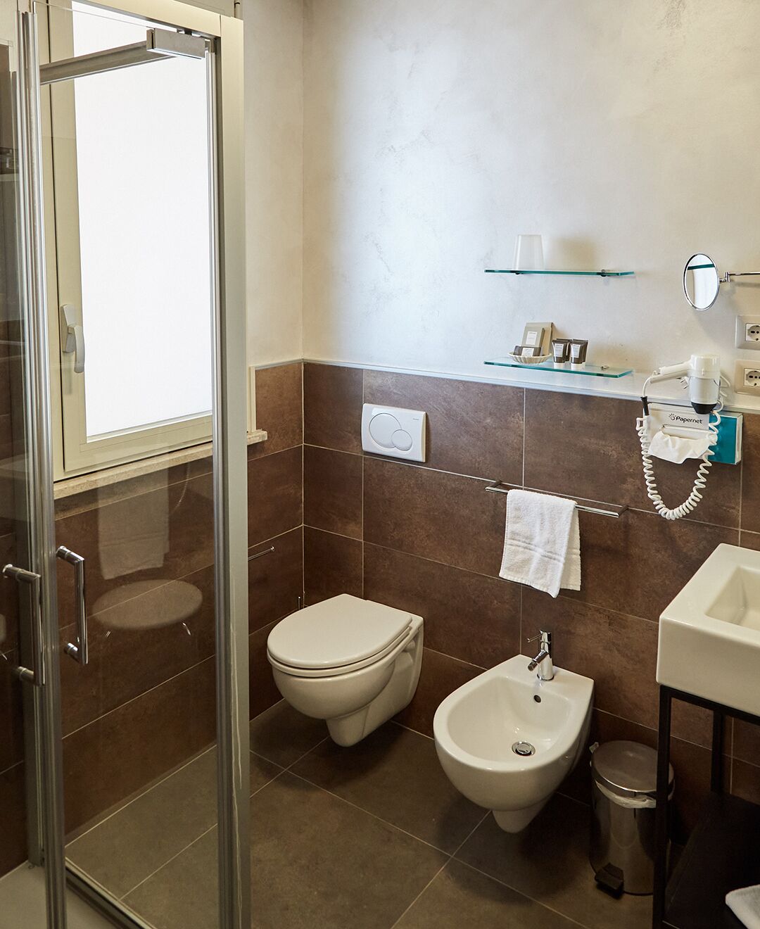 A modern bathroom with a glass shower enclosure, a toilet, a bidet, and a sink.