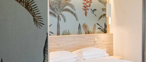 Quarto com cama, roupa de cama branca, cabeceira de madeira e parede com padrão de folha tropical.