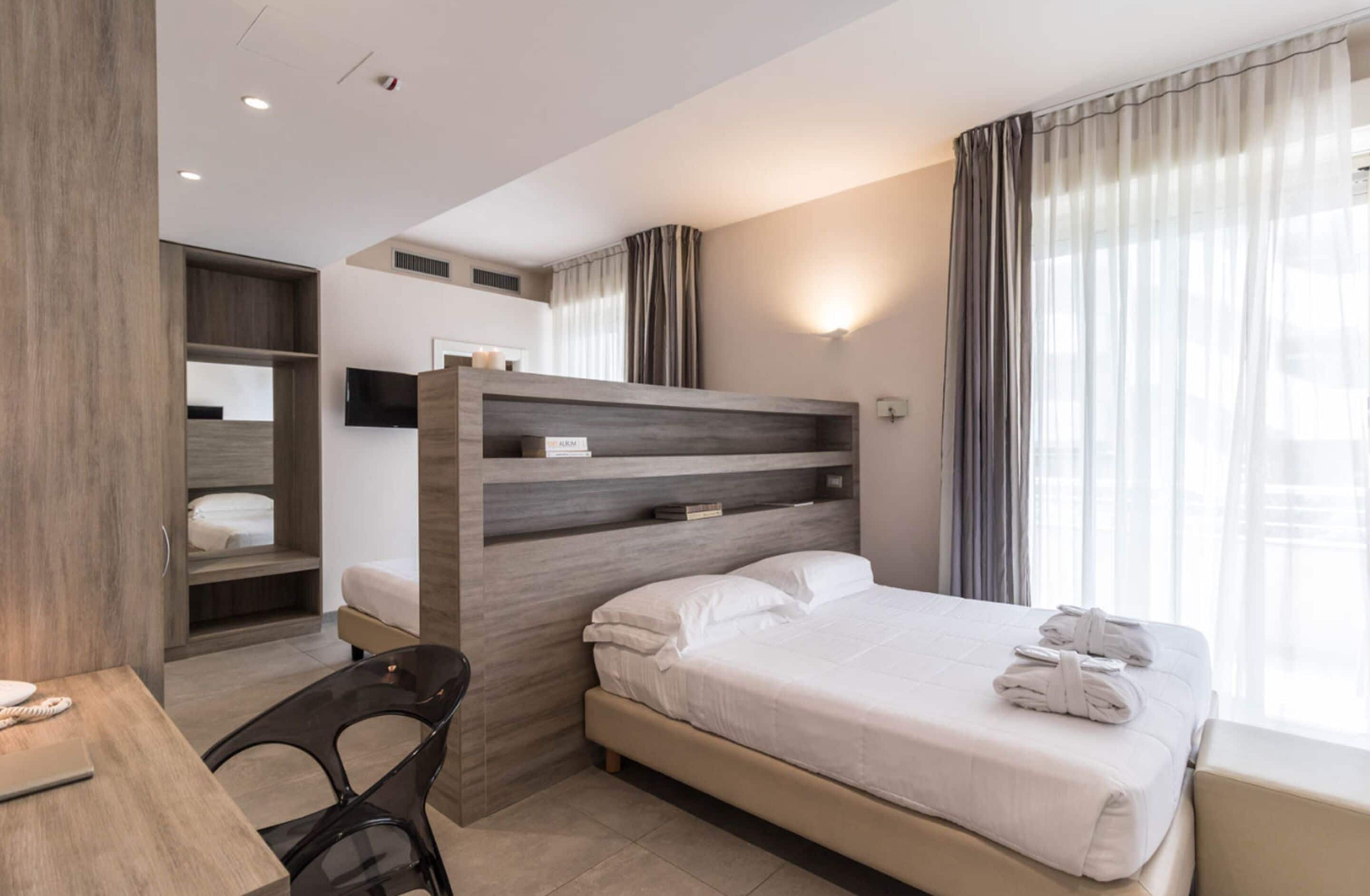 Ein modernes Hotelzimmer mit Bett, Schreibtisch, Stuhl, Kleiderschrank und Fernseher.