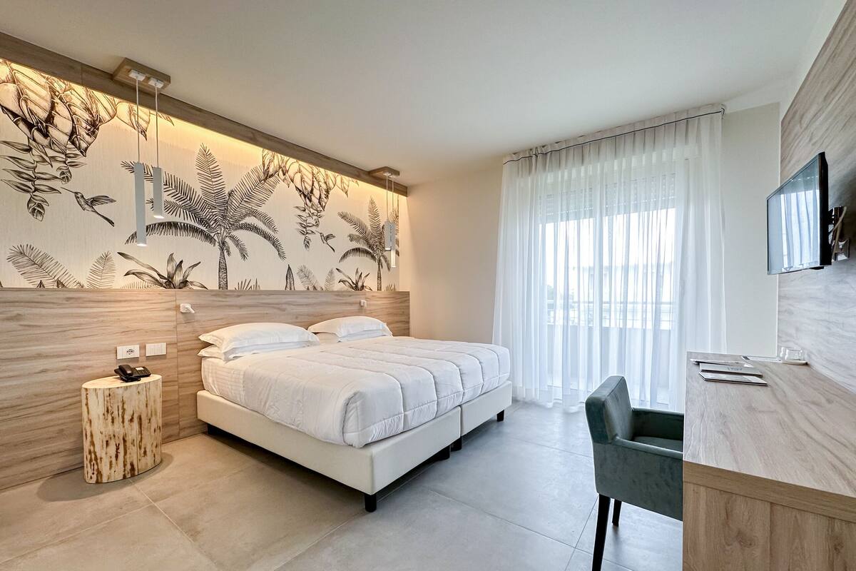 Ein modernes Schlafzimmer mit einem großen Bett, einem Schreibtisch und einem an der Wand befestigten Fernseher.