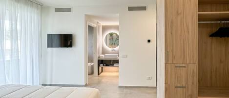 A modern hotel room with a large bed, a wooden wardrobe, a bathroom with a mirror, and a television on the wall.