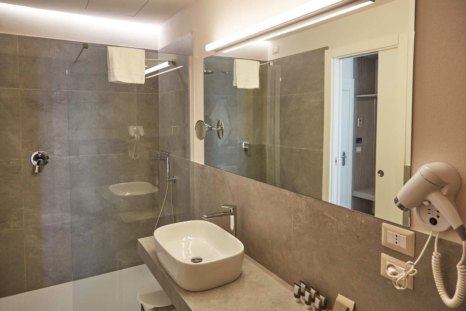 Une salle de bain moderne avec une douche à parois de verre, un grand miroir, un lavabo et un sèche-cheveux fixé au mur.